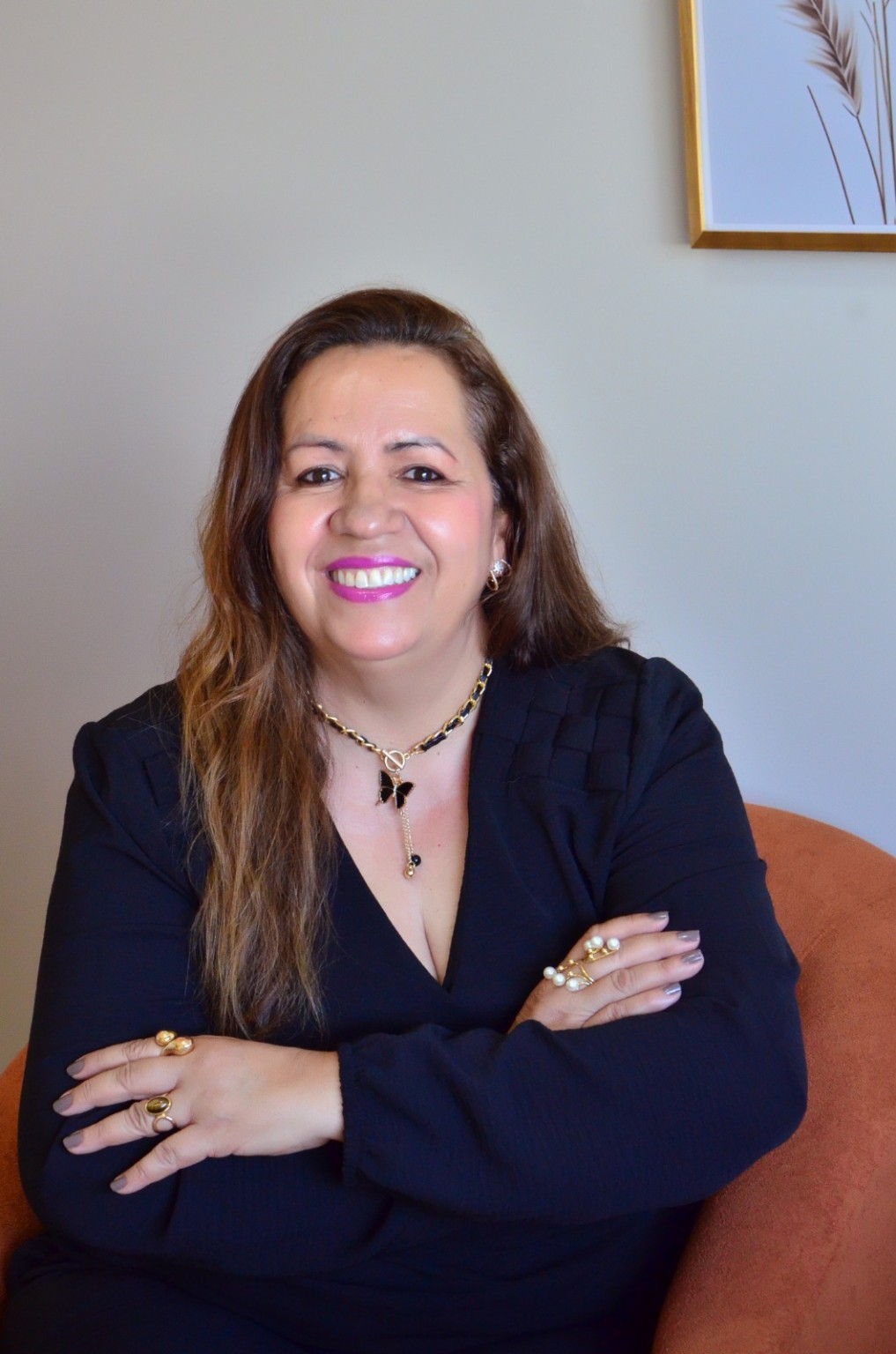 Isabel Ferreira sorrindo, sentada em uma poltrona, com os braços cruzados.